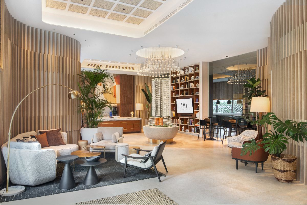 Modern residential lounge with wood accents, indoor plants, chandelier lighting, and comfortable seating
