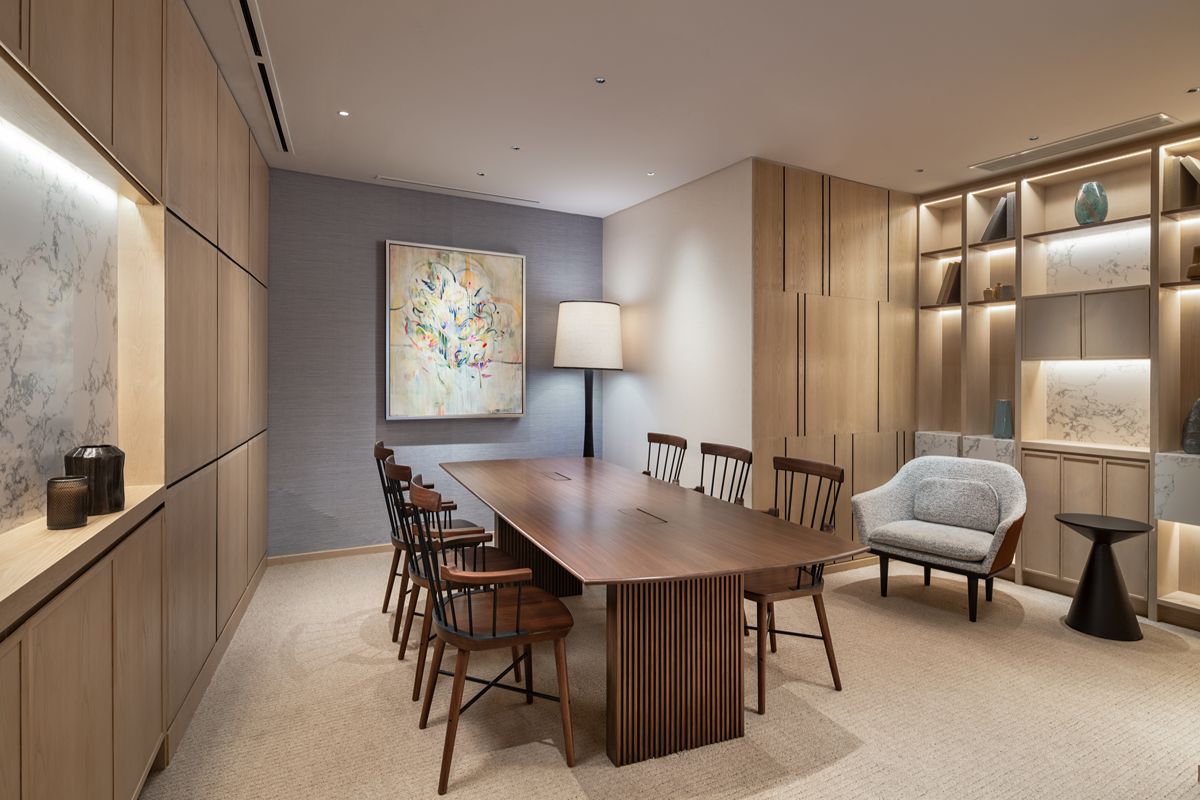 Shared lounge with a long wooden table, matching chairs, a gray upholstered armchair, and illuminated display shelves
